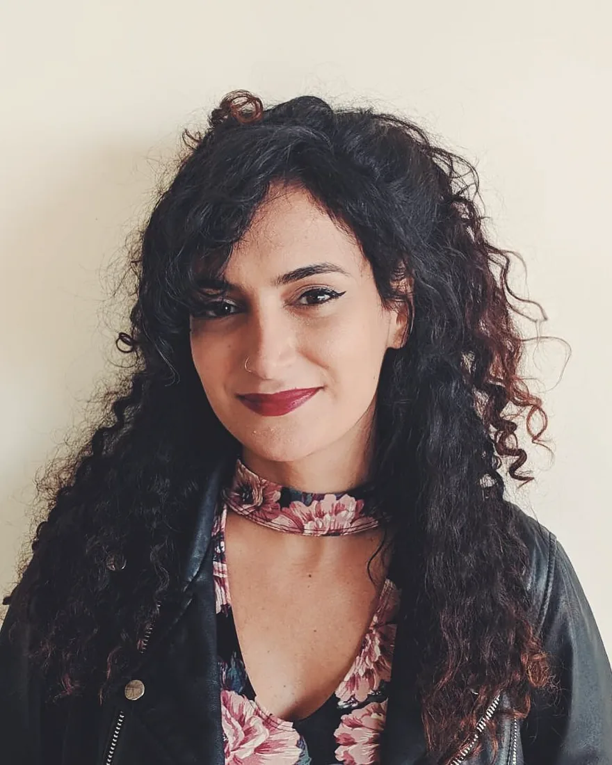 Portrait of Ruba Shamshoum smiling, her long dark curls framing her face